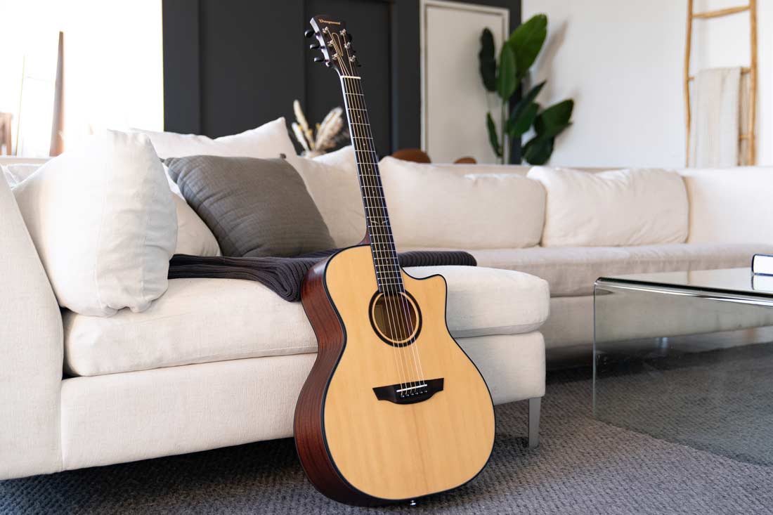 An Orangewood Morgan Spruce guitar leans against a white couch