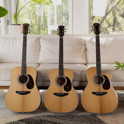 Three Orangewood Topanga guitars with pick guards leaned against a white couch with plants in the background