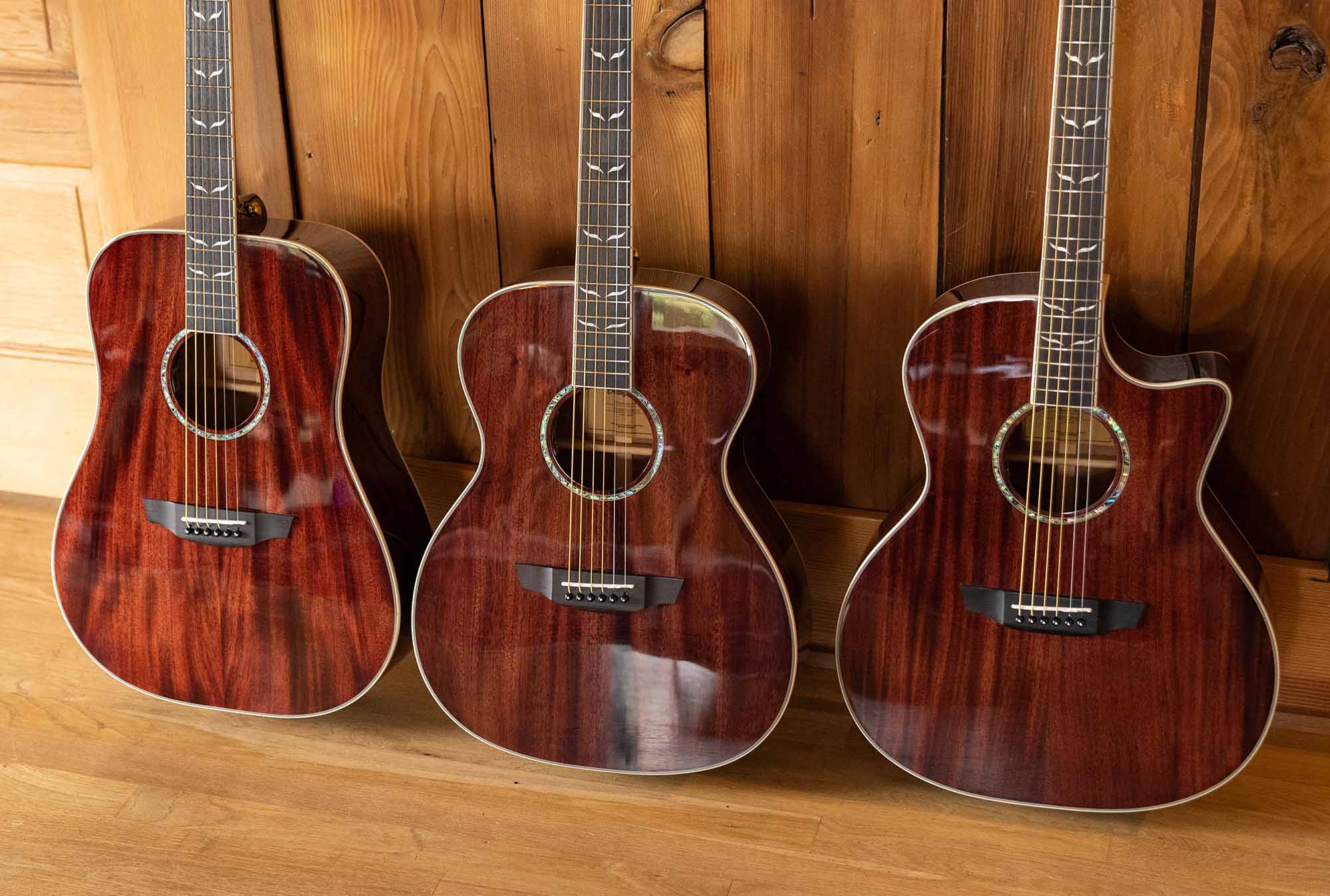 Three solid top mahogany guitars with natural gloss finish in a wood cabin