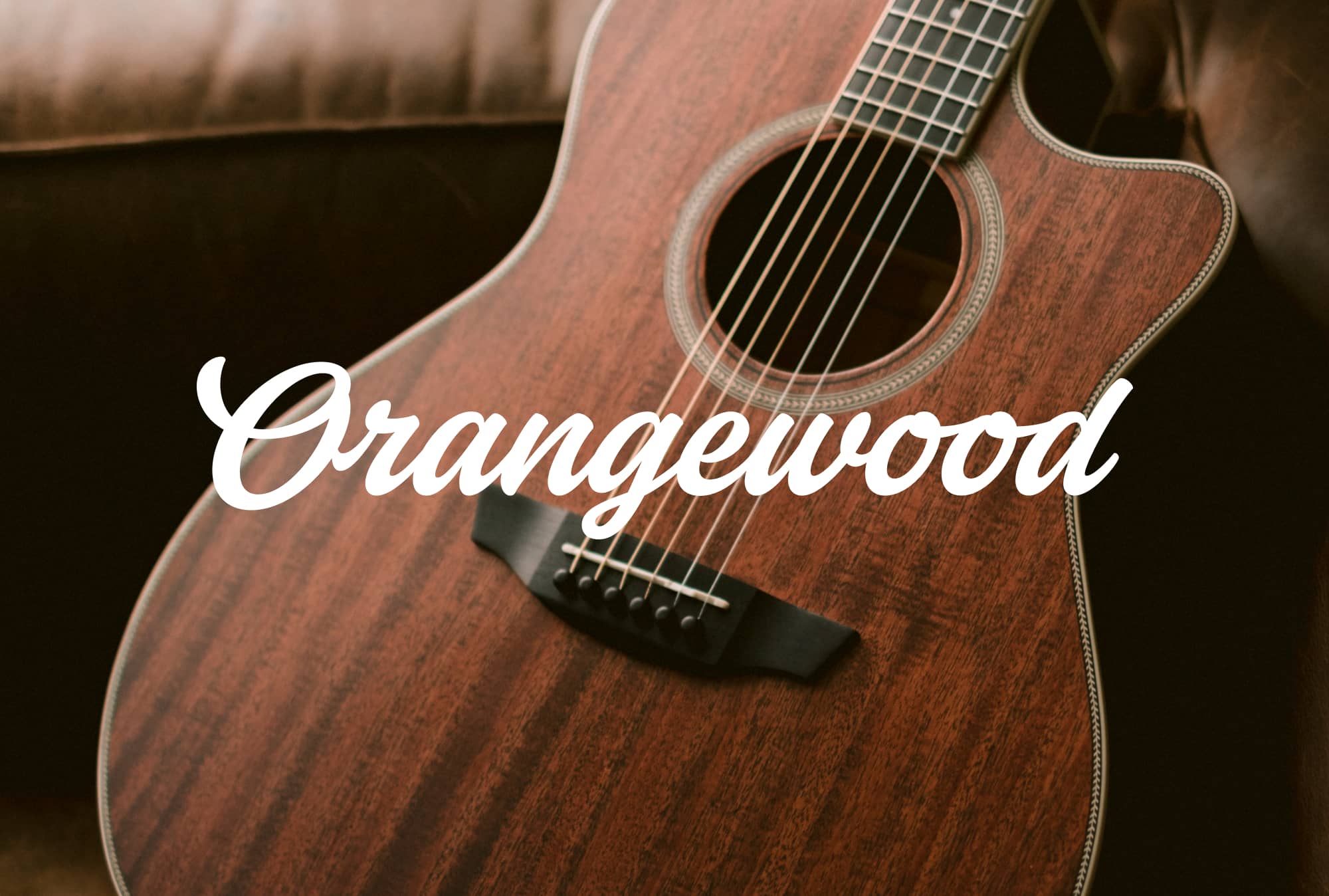 Sage mahogany guitar on a leather sofa with new orangewood logo overlaid