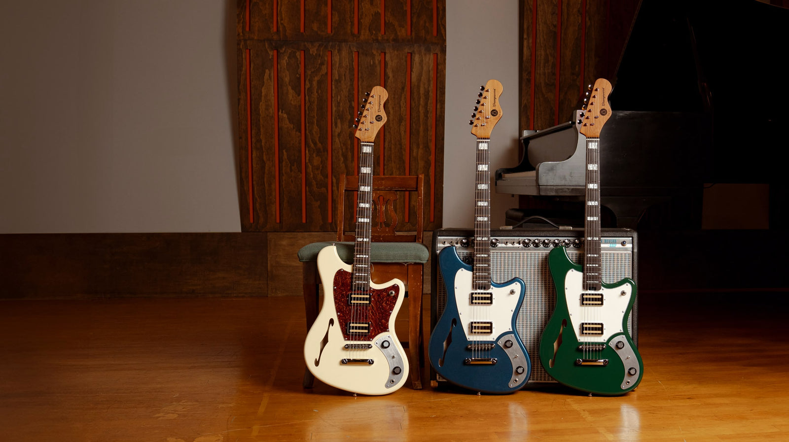 Three electric guitars in different colors standing in front of a amplifier on a wooden floor.