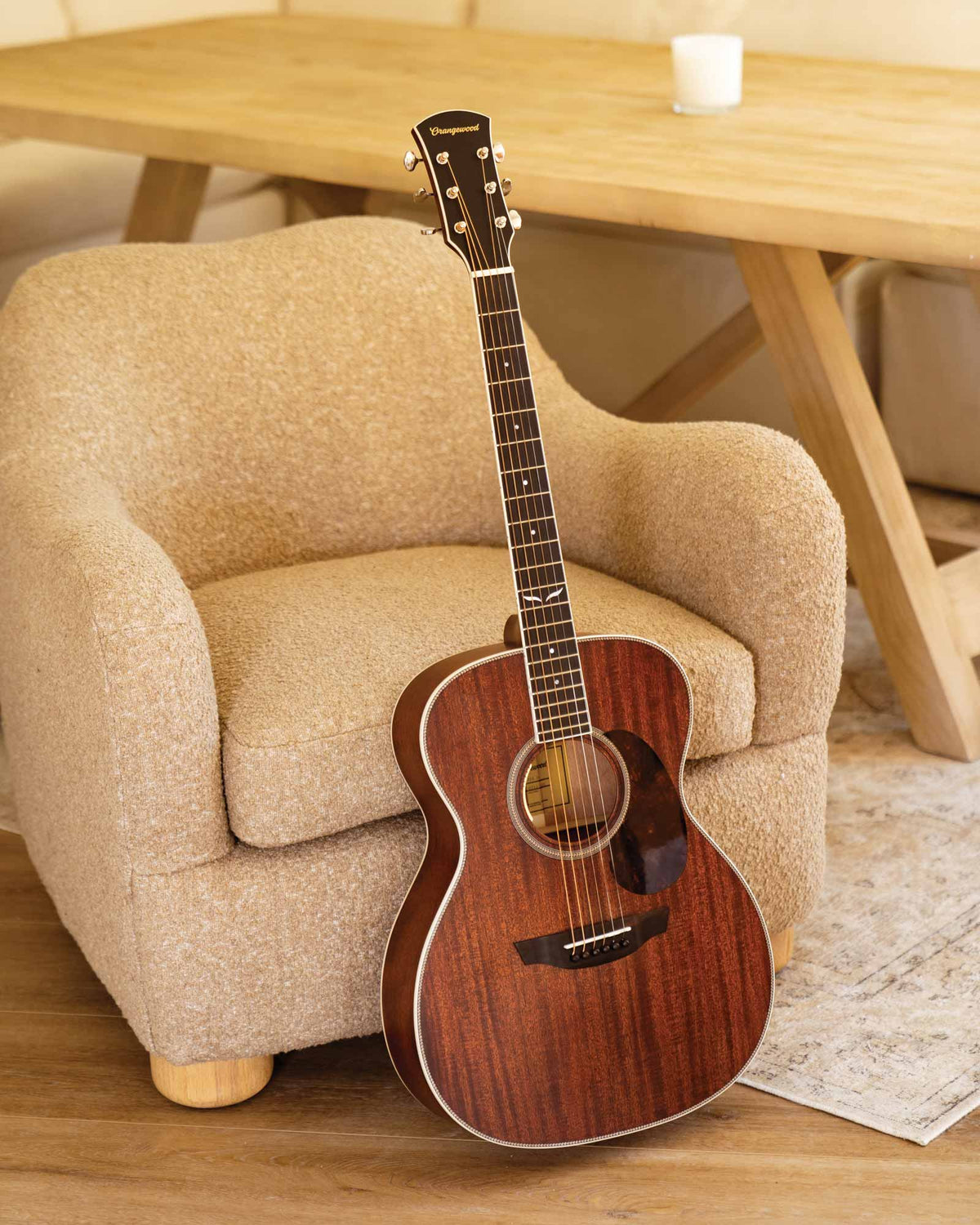 Mahogany grand concert guitar with tortoise pickguard next to a beige chair 