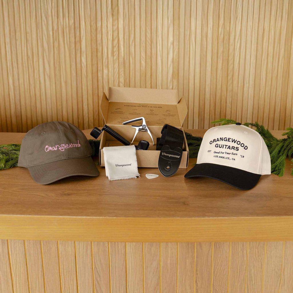 Brown Orangewood script cap and cream Orangewood Guitars cap with accessories on a wooden counter