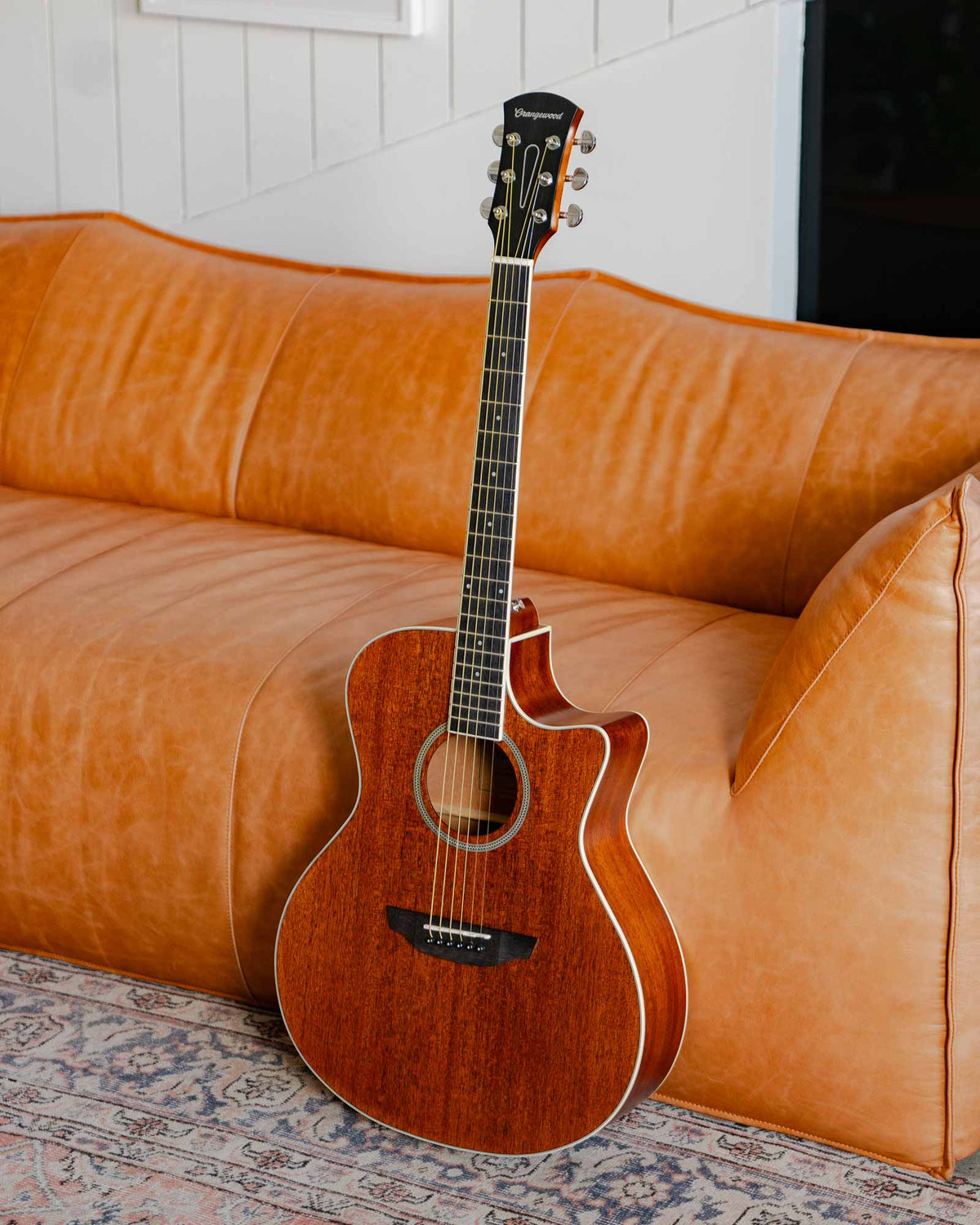 Rey mahogany guitar against a leather sofa