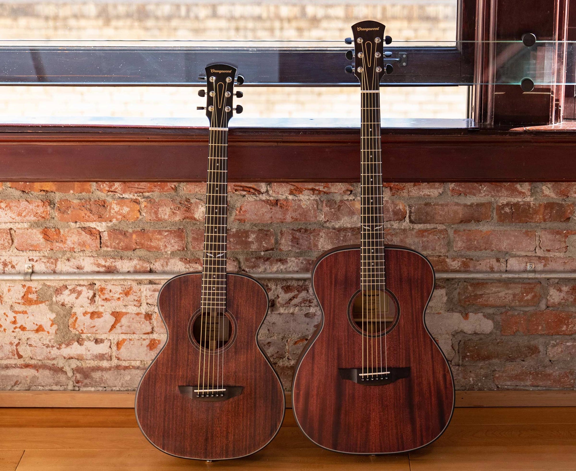 Two Mahogany Orangewood guitars leaned against a brick wall