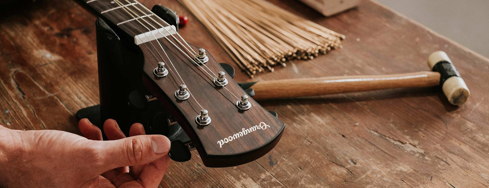 Guitar tech setting up an Orangewood guitar on a workbench with extra strings in the background