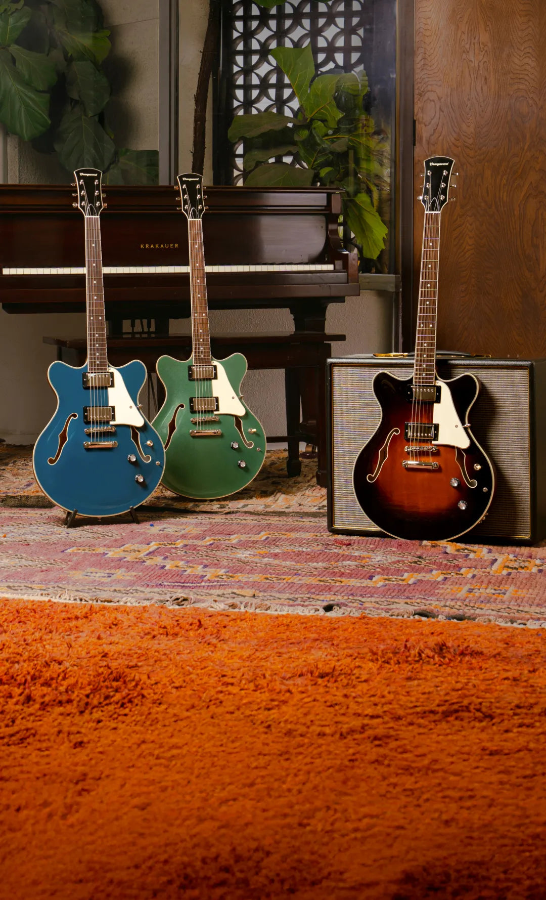 Three electric guitars in front of a piano with a speaker cabinet.