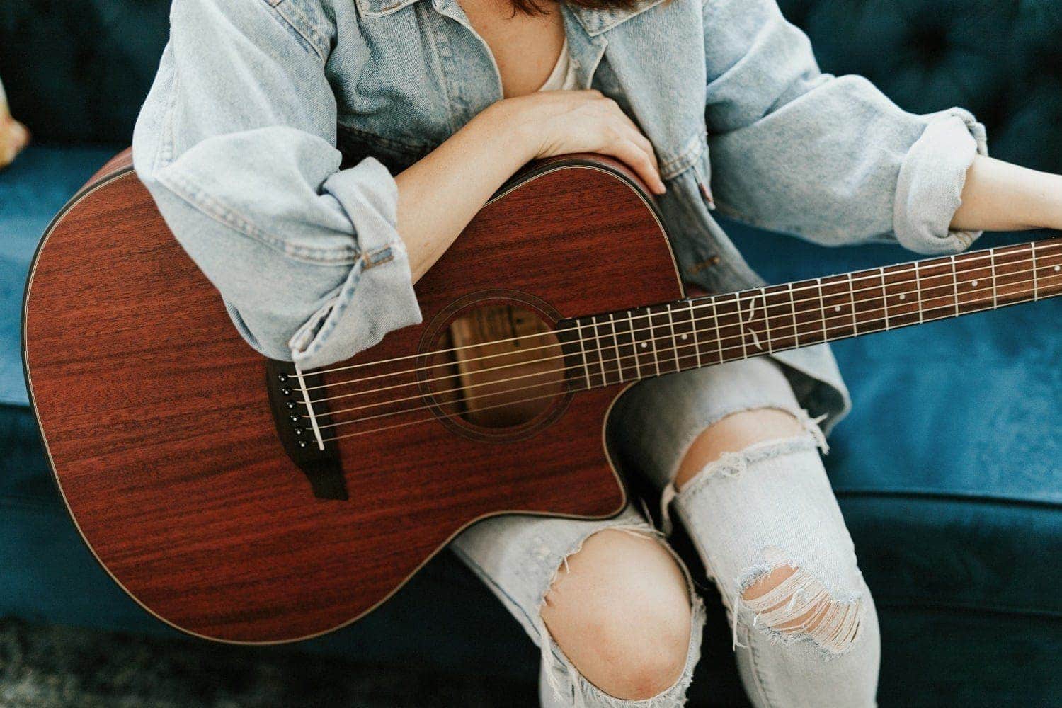 Person holding a morgan mahogany live guitar and sitting on a blue sofa