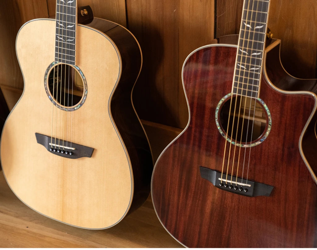 a spruce guitar and mahogany guitar against a wooden cabinet