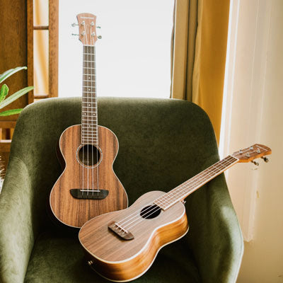 Two Orangewood Marina ukuleles lay on a green velvet chair